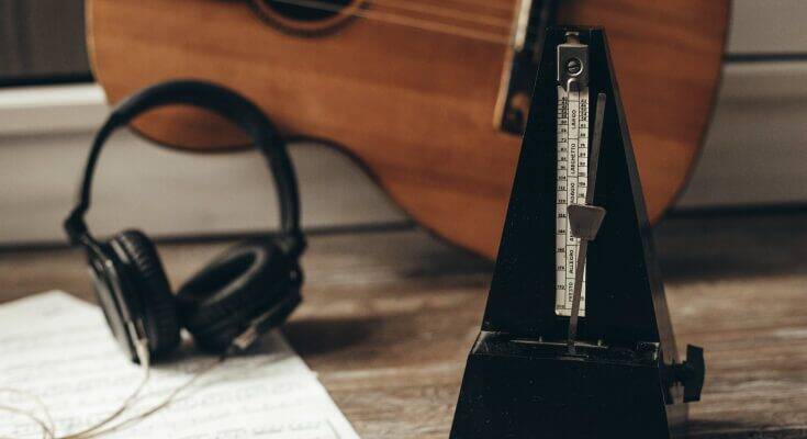 A metronome sits on a table with headphones and a piece of paper behind it.
