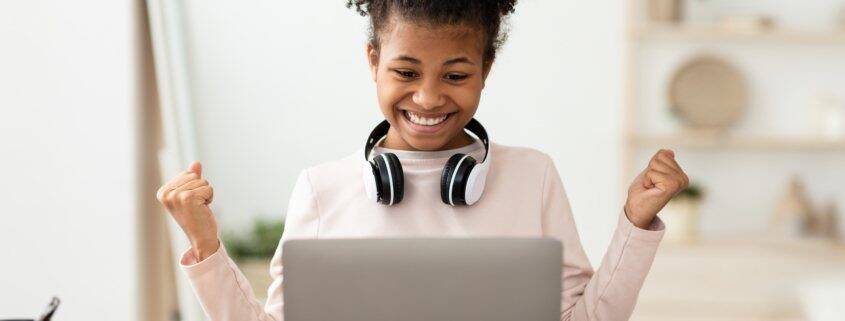 Little Winner. Excited Black Girl At Laptop Gesturing Yes Getting A-Grade During Webinar At Home. Online School Tests Concept