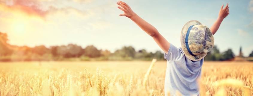 Boy in a wheat field in summer with raised arms watching the sunset