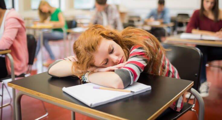 Red-headed teenage girl asleep at her desk during the school day