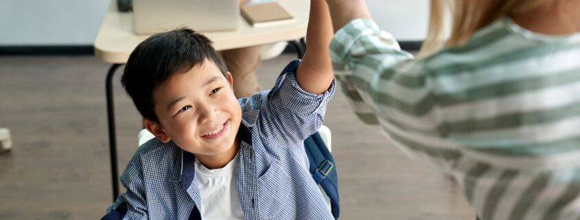 Young male student of Asian heritage smiles as he high-fives his academic coach standing in front of him.