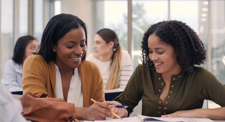 Two black students collaboratively reviewing their homework, deeply engrossed in their academic discussion and learning from each other.