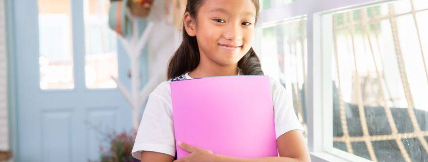 Little asian girl smiling and holding books at home